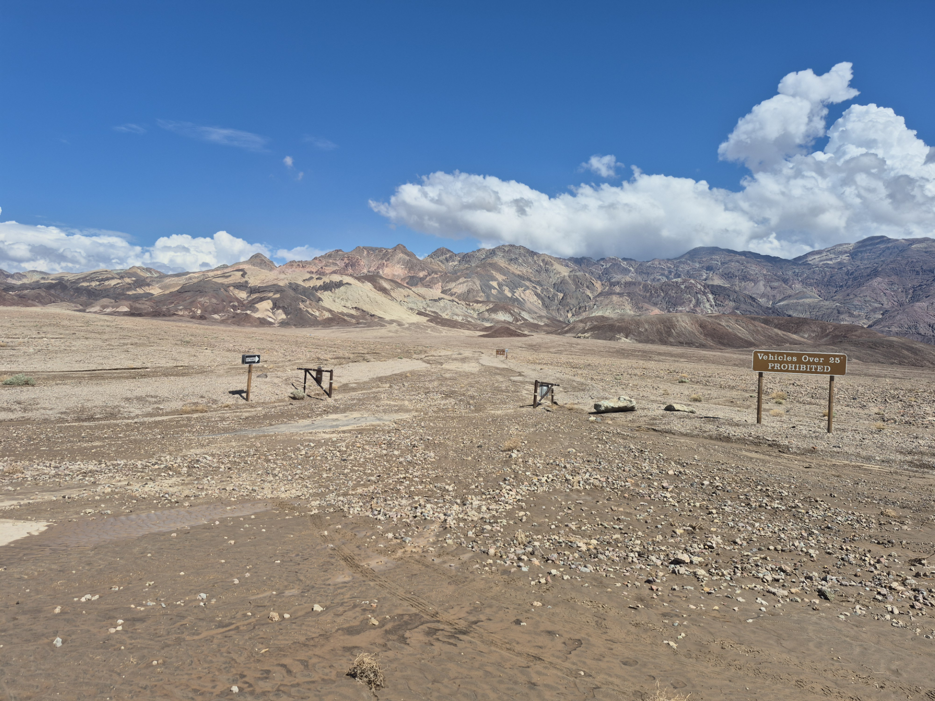 Brown dirt and rocks cover the landscape with distant bare mountains. Only signs and gates show that there was a road here.