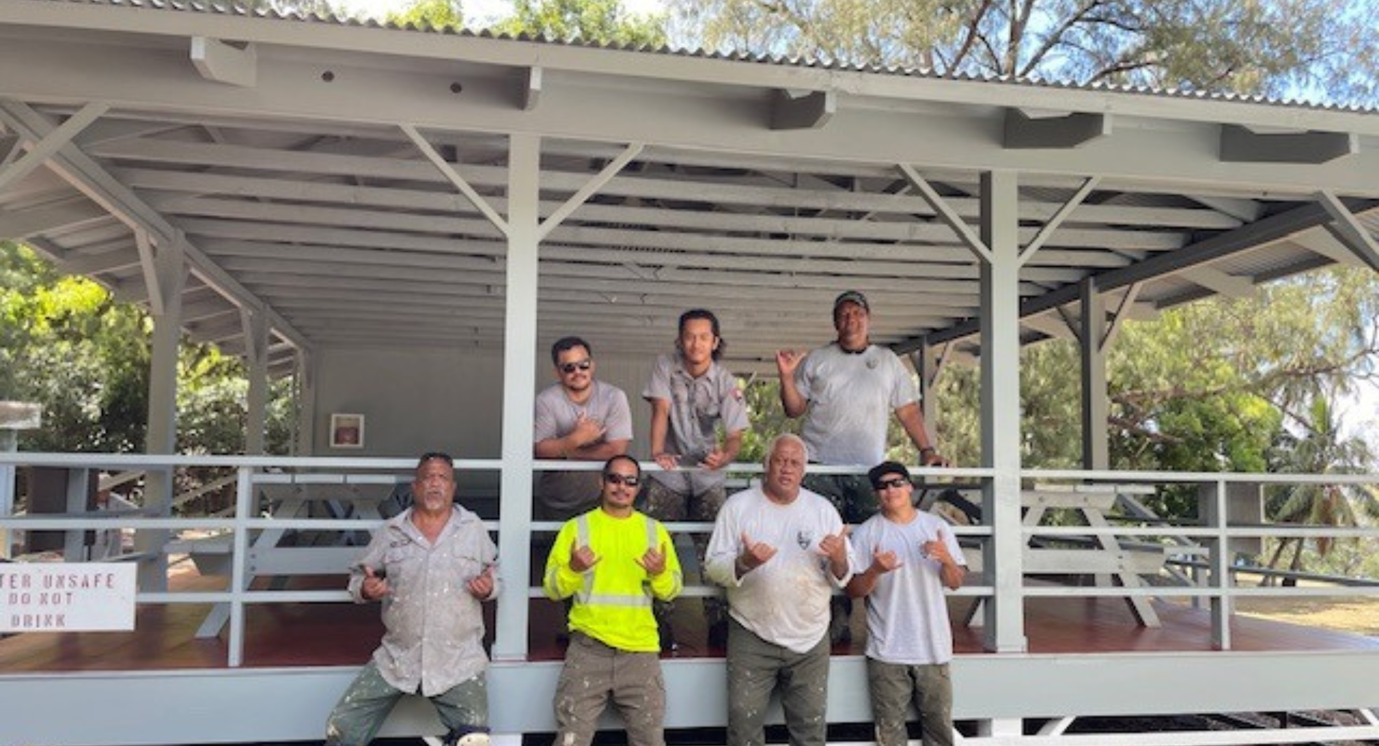 Outdoors; older pavilion in cut grass lawn with trees and blue sky behind.