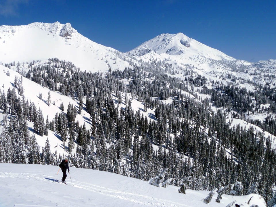 A landscape photo of a skier below two snow-covered volcanic peaks.