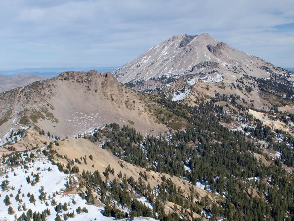 A landscape photo of a skier below two snow-covered volcanic peaks.