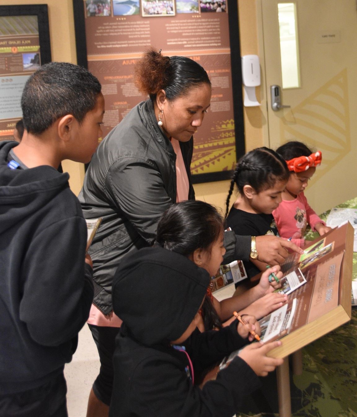 Indoors; Inframe five children and one adult working on books in exhibit area.