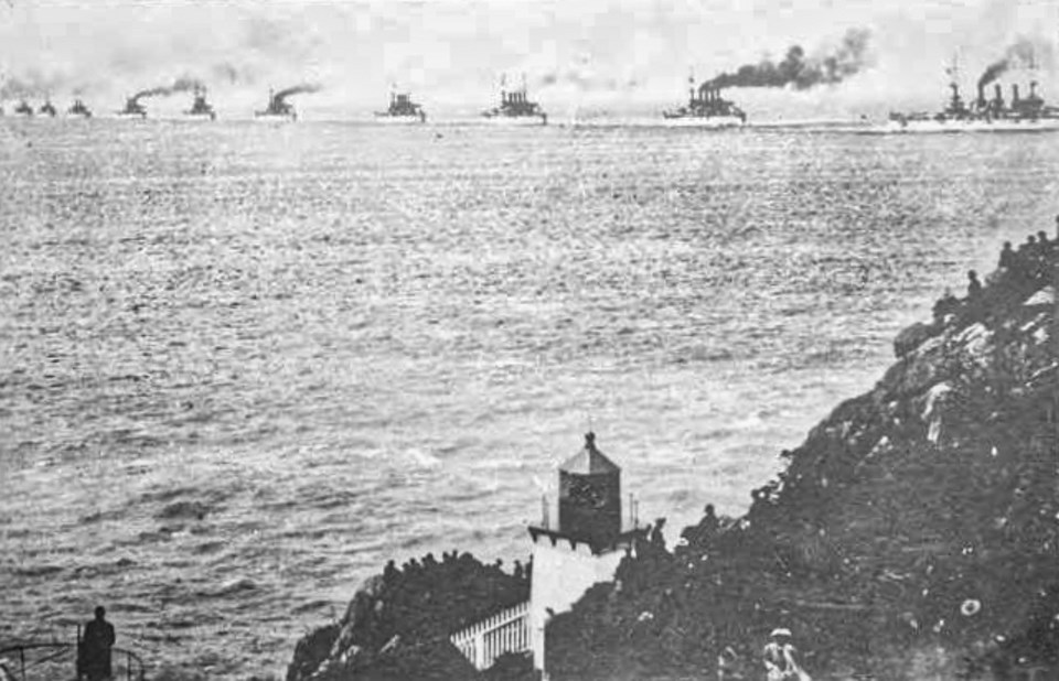 Naval ships lined up on ocean passing lighthouse