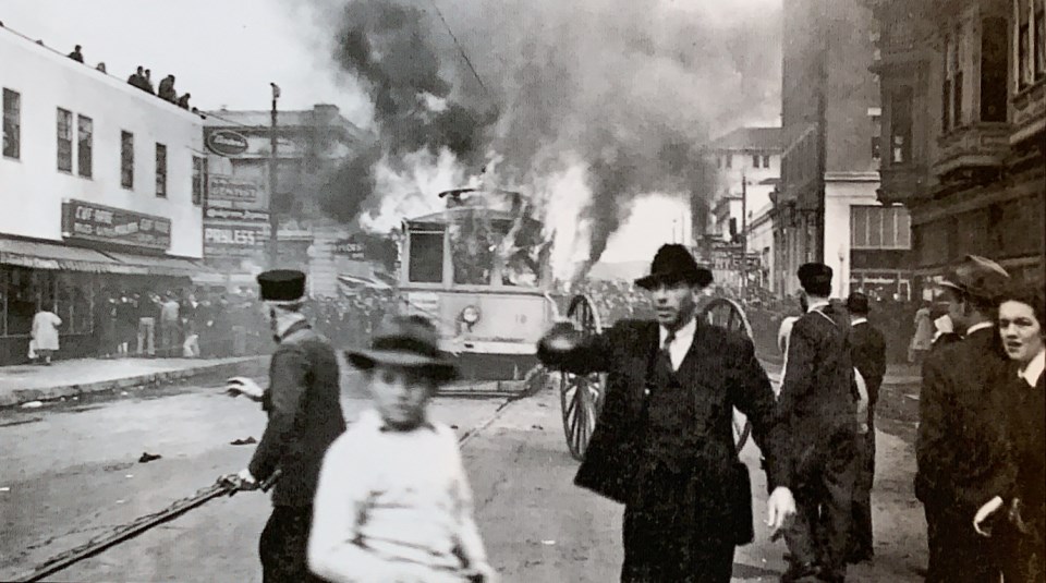 People standing on street with trolley car burning in background