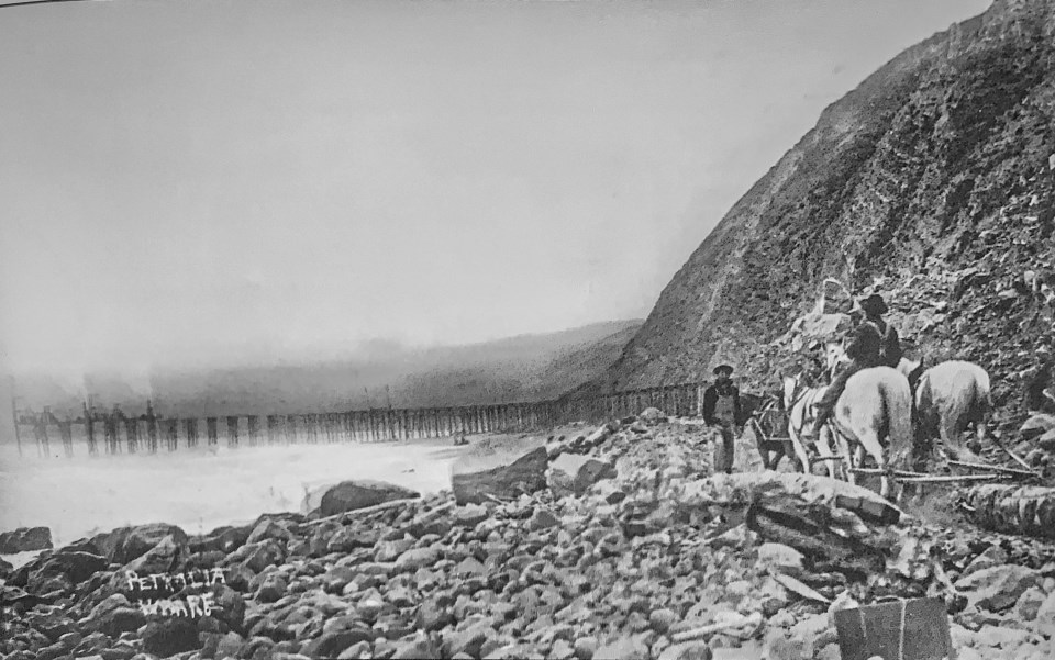 Horses and men ride along bluff with wharf in ocean