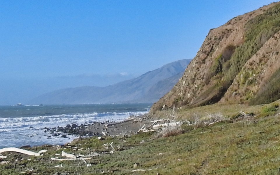 Horses and men ride along bluff with wharf in ocean