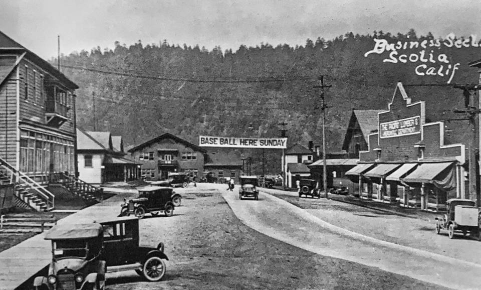 Street with old cars and buildings, hillside in background.