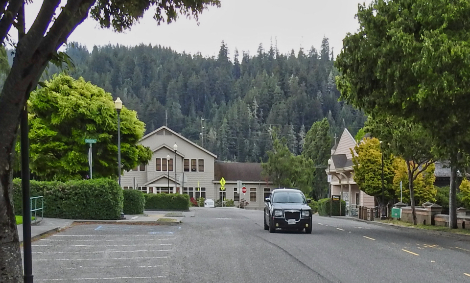 Street with old cars and buildings, hillside in background.