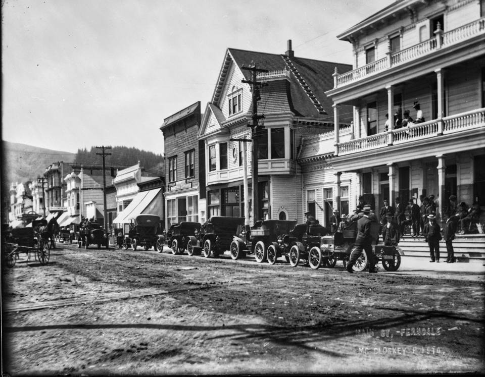 Old automobiles on dirt street in front of buildings