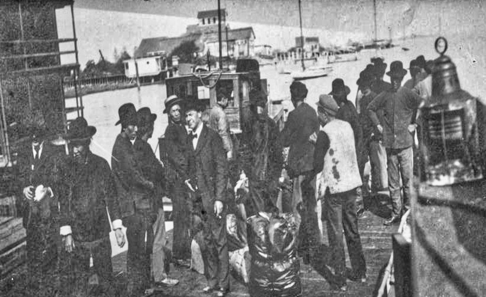 A group of men on a wooden dock with buildings in background