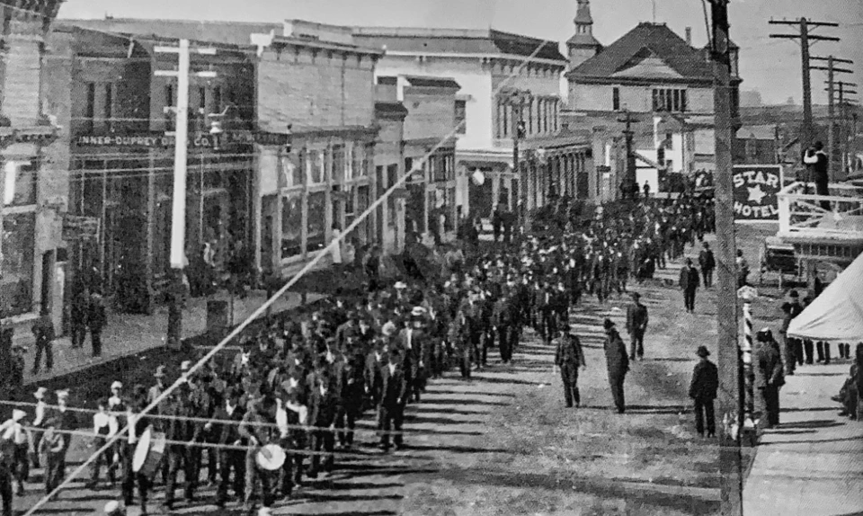 People march in a large group down a city street.