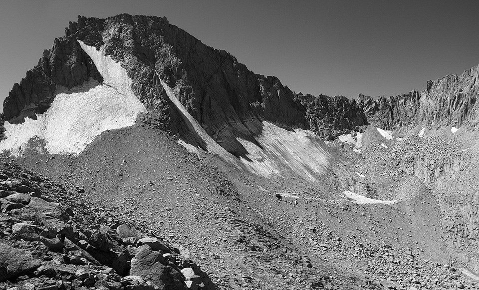 Rocky mountain slope mostly covered with a glacier that stretches out to both sides and has a chute stretching down toward lower righthand corner of photo.