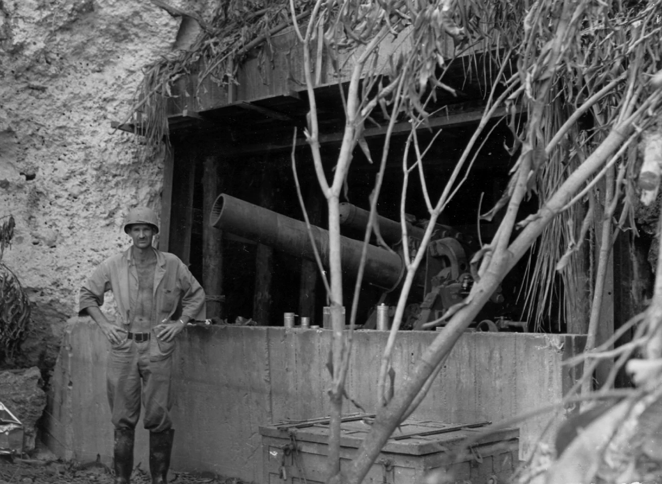 Black and white photo of a solider standing next to a bunker with a very large gun
