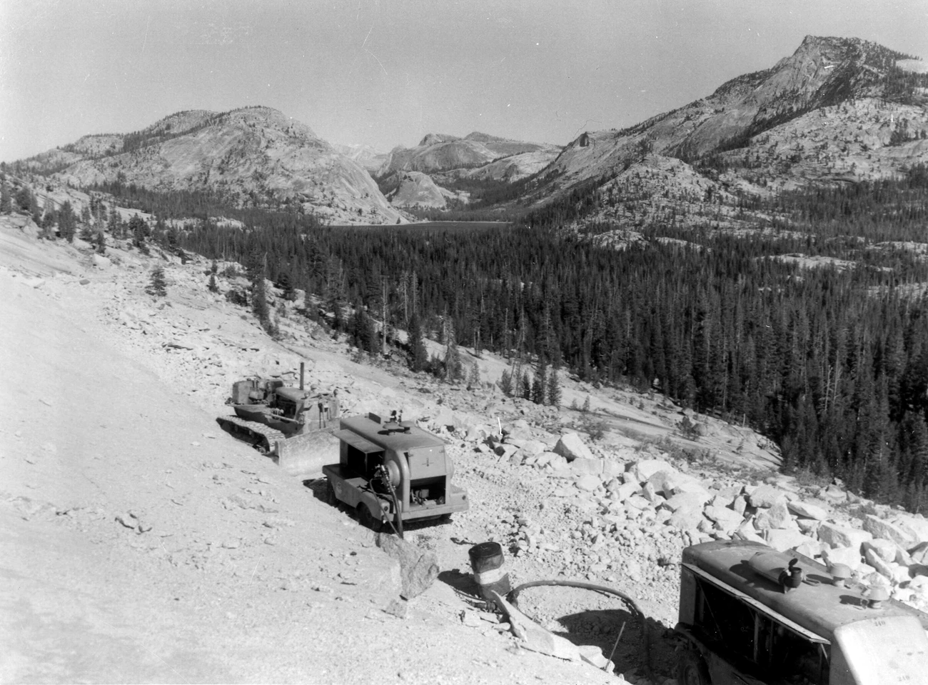 A steep granite slope in the foreground, with forest, peaks, domes, and a large lake in the distance