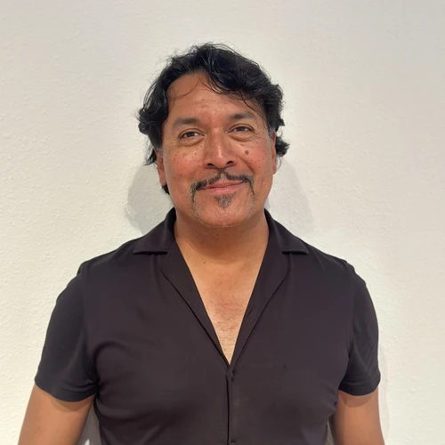 A man in a black shirt stands in front of a blank wall. 