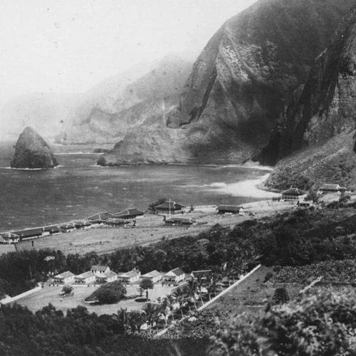 Outdoors; black and white photo of structures and complex by ocean and cliffs.