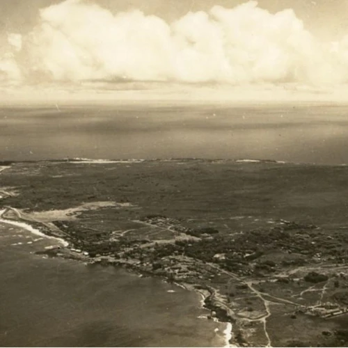 Outdoors; sepia photo of aerial view of a peninsula jutting into the ocean with cloudy sky above.