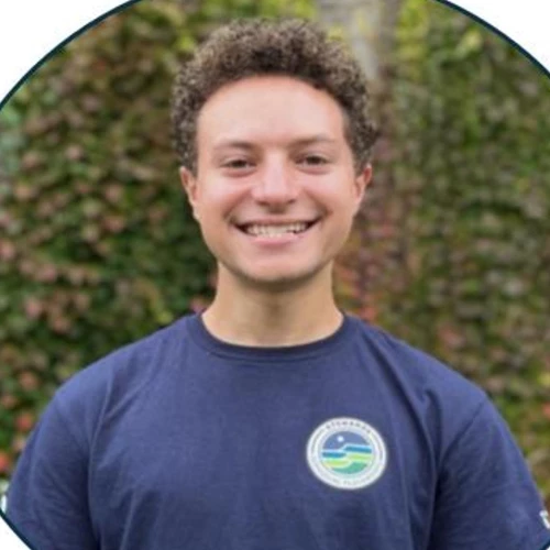 Portrait of a young adult wearing a navy blue tshirt uniform in front of an ivy covered wall