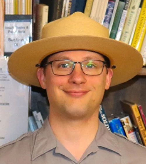 A ranger in a flat hat looks at the camera.