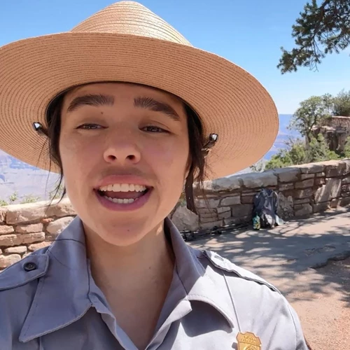 A ranger stands in front of a rock wall lining the rim of the Grand Canyon.