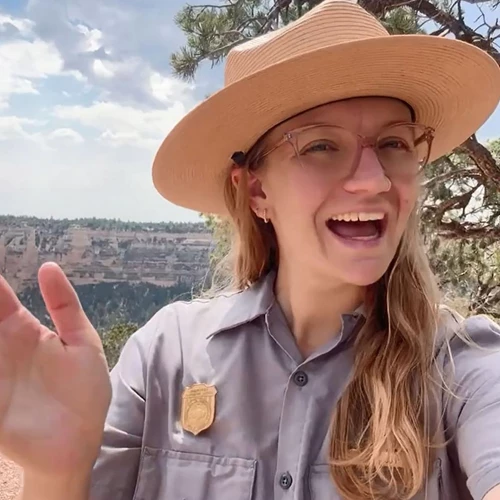 A ranger waves their hand in front of a tree on the Grand Canyon rim.