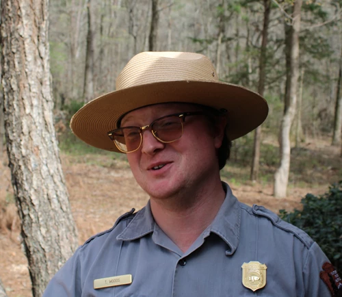 A park ranger in a flat hat with trees in the background.
