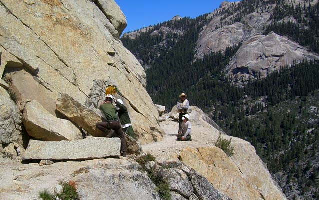 Trail crew members remove rockfall on a cliffside trail.