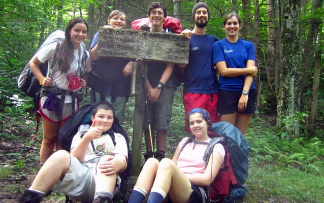 A group of young backpackers poses by a trailhead sign in the park.