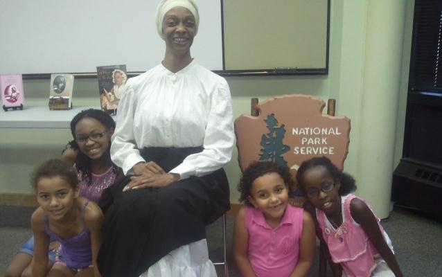 Denise Valentine, portraying Phillis Wheatley, sits with young girls after her writing program