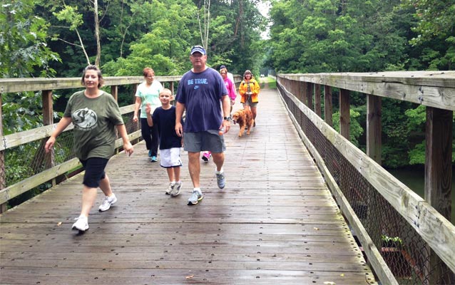 A family walks across a wooden bridge in a forest