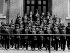 Children stand in suits in front of a schoolhouse