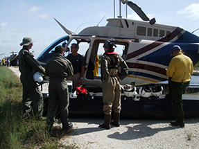 A group standing by a helicopter receives a safety briefing.