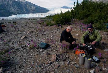 two people sitting on rocky ground near a glacier