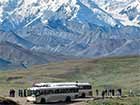 people standing near a bus, looking at snowy mountains in the distance