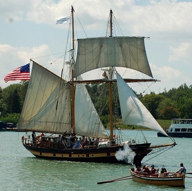A rowboat approaches a two-masted sailing ship flying the American flag. A rowboat approaches a two-masted sailing ship flying the American flag.