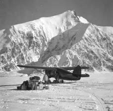a plan on skis parked on a snowy field near a craggy white mountain a plan on skis parked on a snowy field near a craggy white mountain