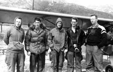 five men standing next to a small propeller aircraft