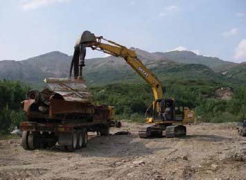 large backhoe placing metal debris into a dump truck