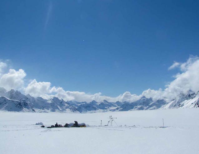 a vast snowy field with people on it, surrounded by snowy mountains