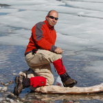 man kneeling by a partially frozen river or lake