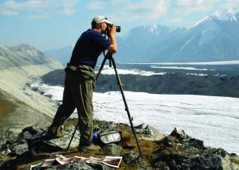 man standing on a ridge taking photos of a glacier man standing on a ridge taking photos of a glacier