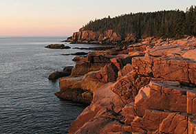 Sun rises and illuminates rocky cliffs and the ocean with a warm glow Sun rises and illuminates rocky cliffs and the ocean with a warm glow