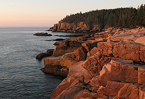 Sun rises and illuminates rocky cliffs and the ocean with a warm glow