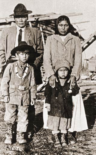 black and whit ephoto of man, woman and two young children in front of a log cabin