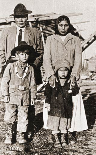 black and whit ephoto of man, woman and two young children in front of a log cabin black and whit ephoto of man, woman and two young children in front of a log cabin