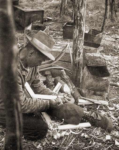 man kneeling amid wood shavings, fitting pieces of wood together