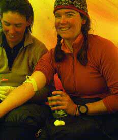 two women sitting in a tent, one drawing blood from the other