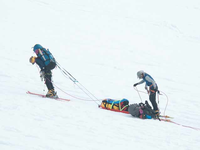 two mountaineers skiing up a slope, pulling a sled