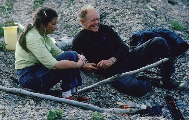 man and woman sitting on the ground by a small campfire