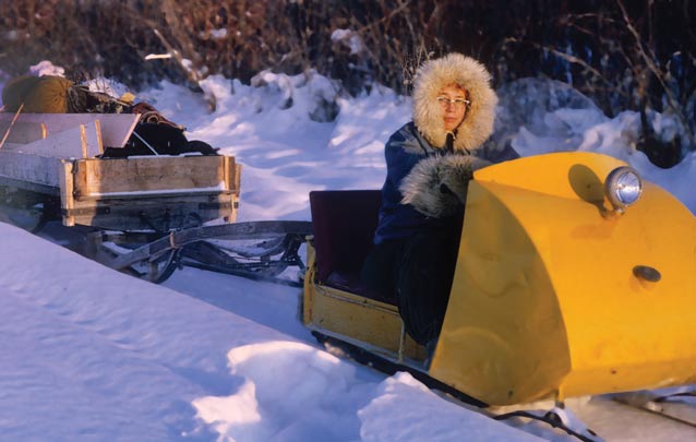 woman driving an old snowmobile, pulling a sled