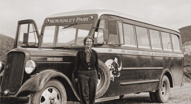 black and white historic image of woman standing near a bus